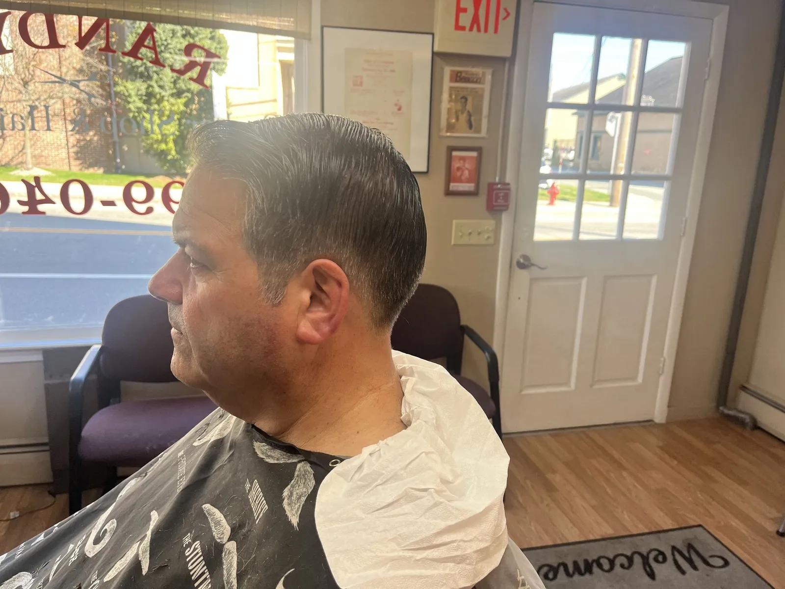 Side profile of a man with a slicked side part and tapered sides, sitting by the shop window