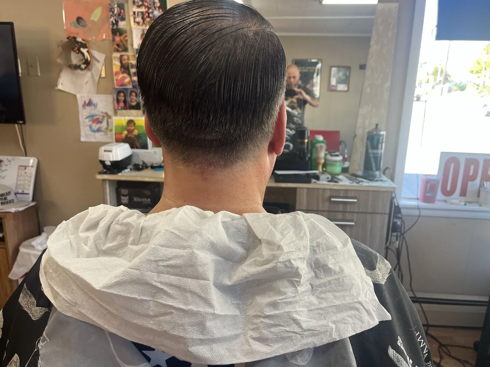 Back of a man's head with dark hair combed back and a soft tapered neckline
