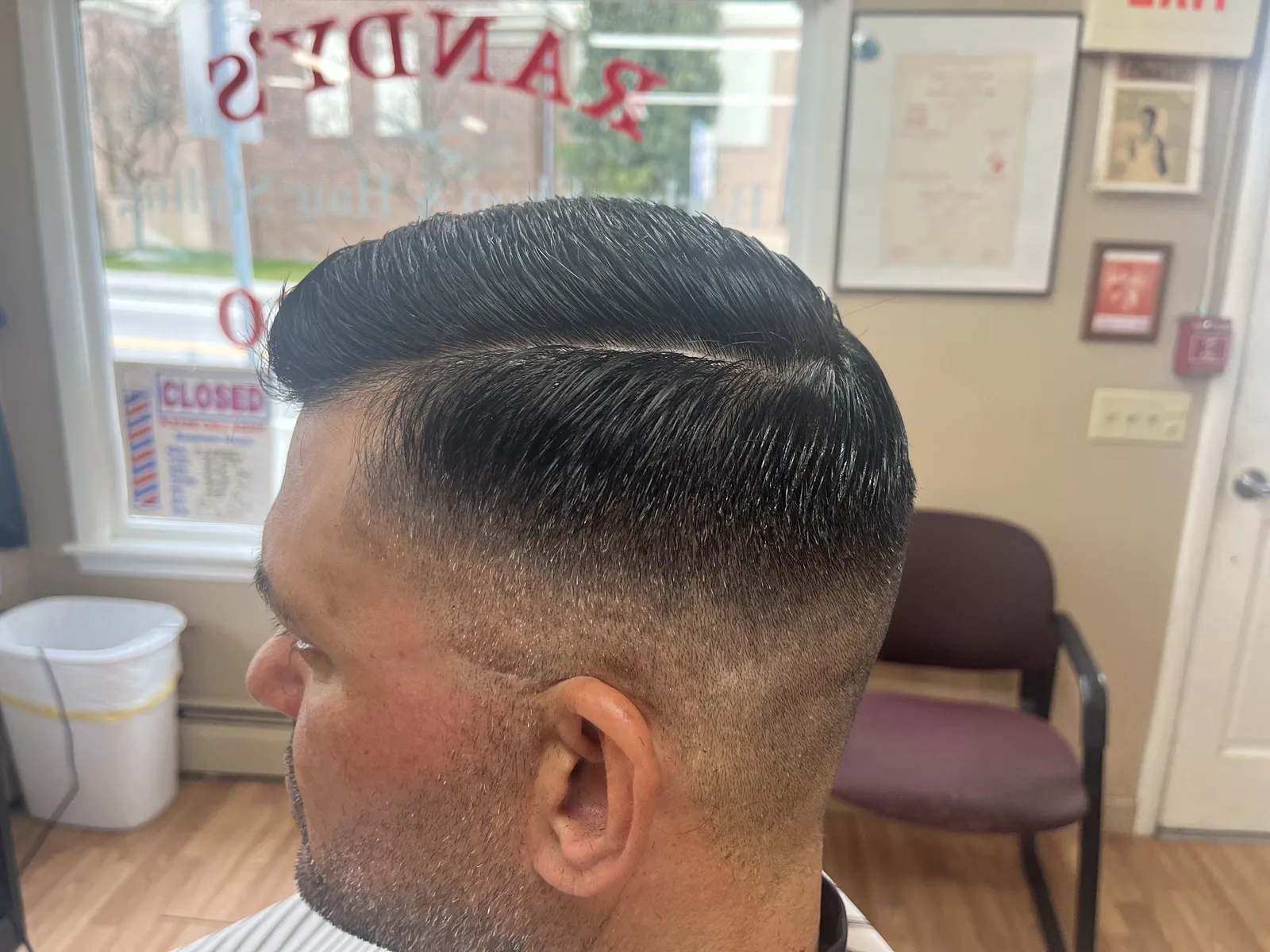 Close side view of a dark, slicked comb over with a hard part and a mid fade