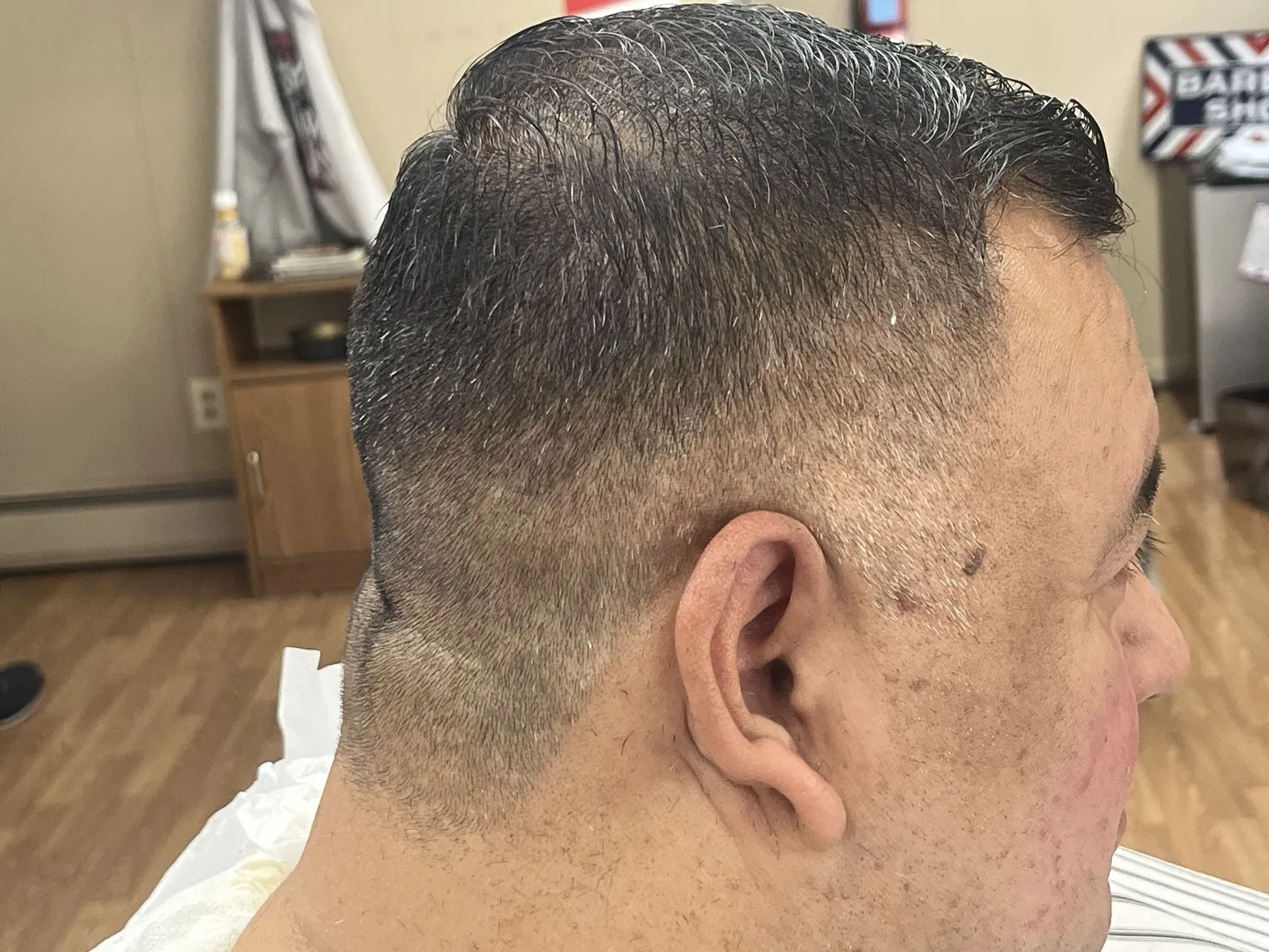 Close side view of short grey-flecked hair with a low taper behind the ear