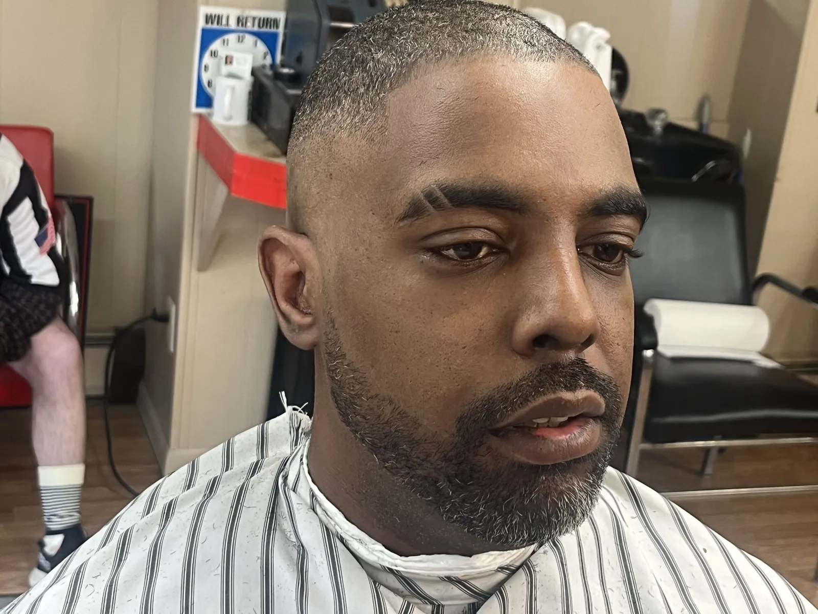 A man with a short buzz cut, a sharp hairline lineup, eyebrow slits and a lined beard