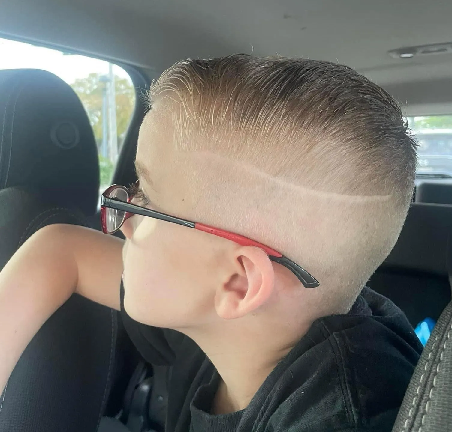 A boy in glasses with a slicked top, a shaved part line and a skin fade